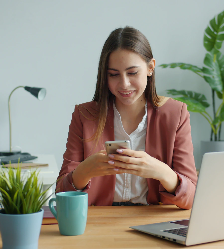 Smiling woman at her desk booking a salon appointment on her phone